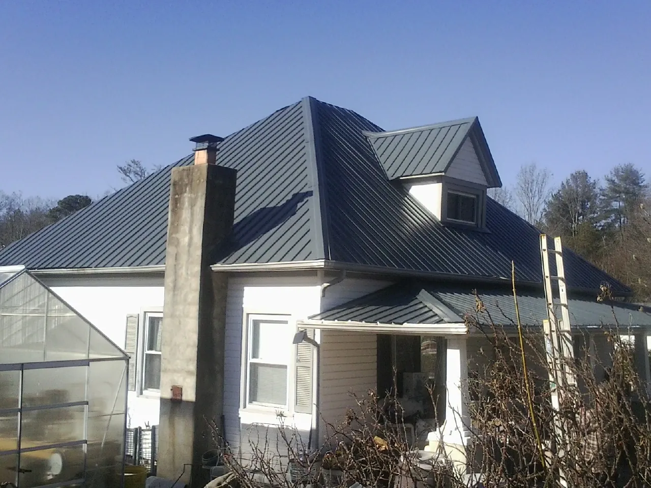 Dark blue standing seam metal roof on a white farmhouse with dormer — Slate & Tile Roof Repair by Roofing Brothers in Taft