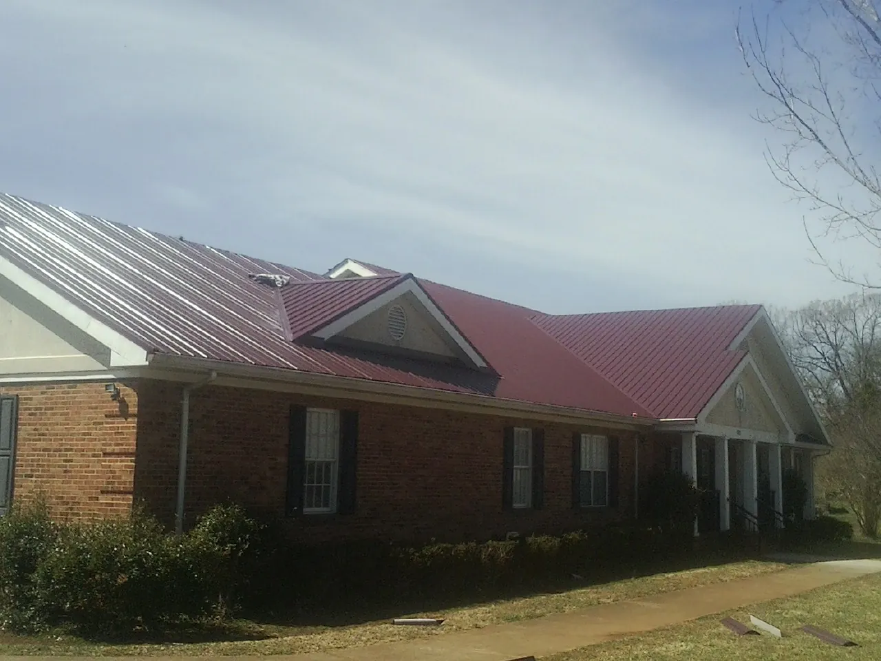 Red metal roof with gabled entries on a long brick building, from a Hail Damage Roof Repair job in Taft