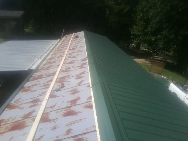 Old rusted panels beside newly installed green metal roofing — Wind Damage Roof Repair by Roofing Brothers in Taft