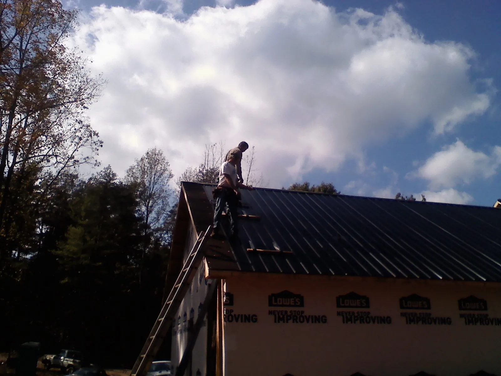 Roofer fastening dark metal panels high against a cloudy sky, from a Roof Inspection job in Taft